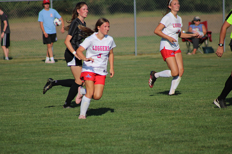 Two LLCC women's soccer players run across the field with a player from the opposing team directly behind them.