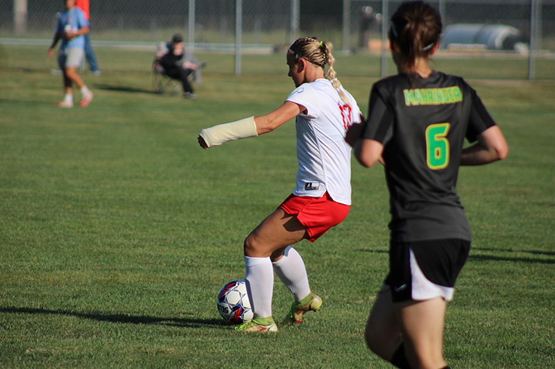 An LLCC women's soccer player kicks the ball while a player from the opposing teams runs toward her.