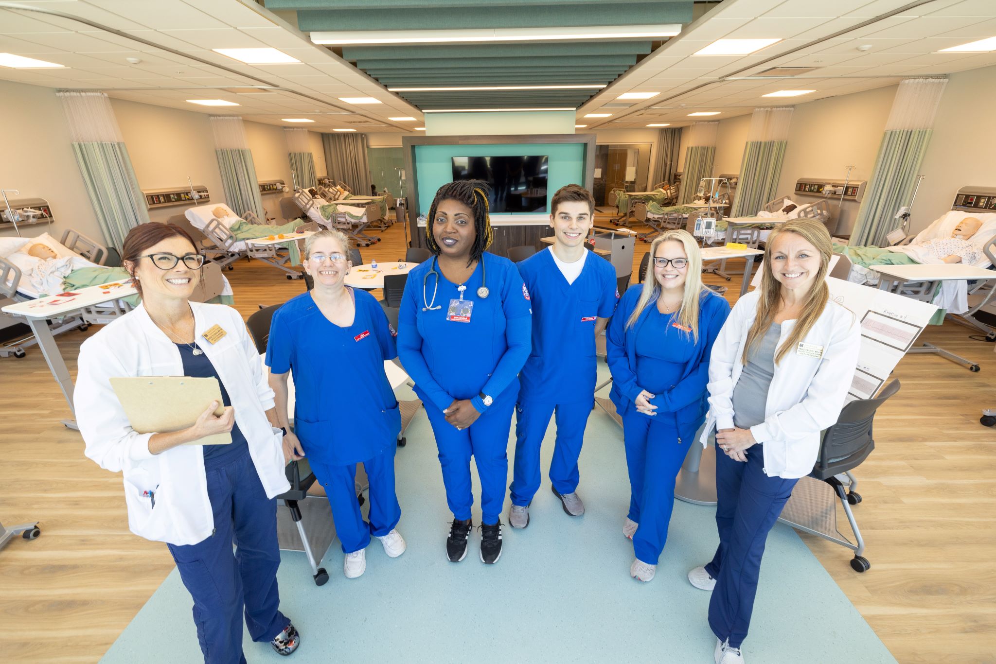 four nursing students in blue scrubs pose with their nursing instructors.