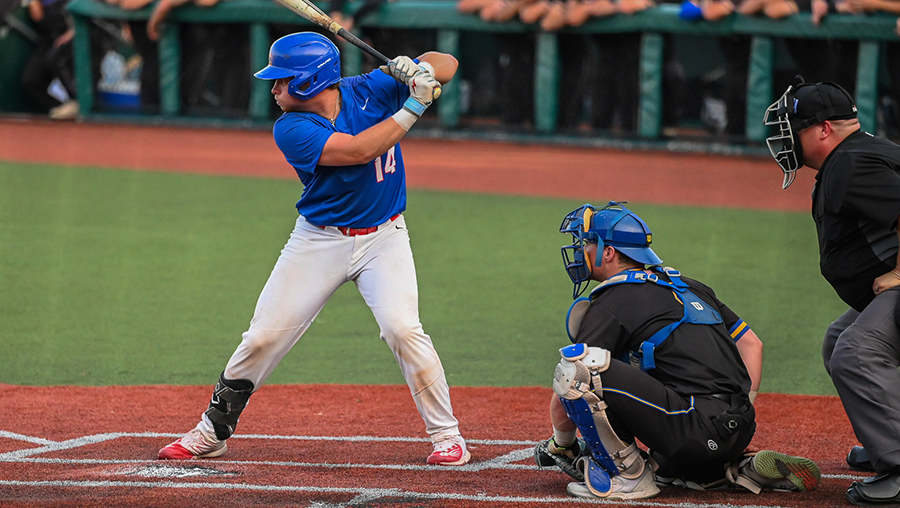 A Loggers baseball player stands ready to bat at the plate, with the catcher and umpire positioned behind.