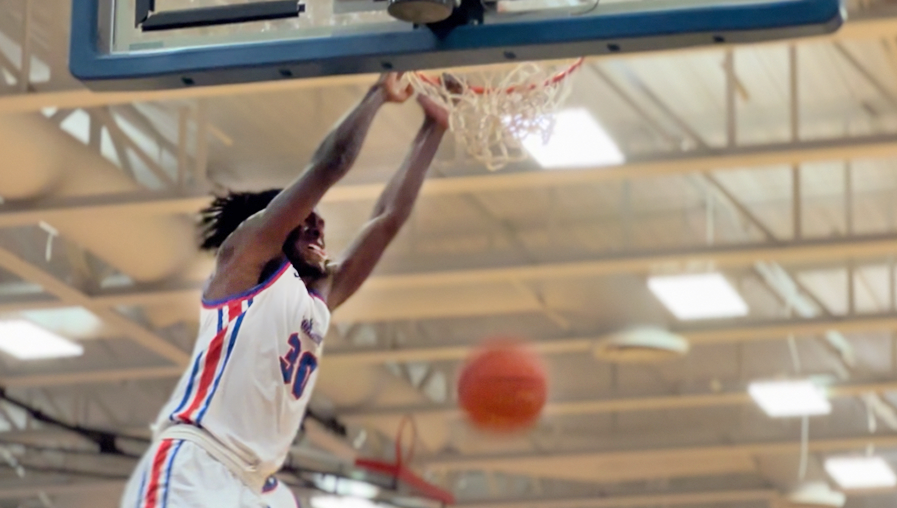 A Loggers basketball player slam dunks a ball and hangs on the rim.