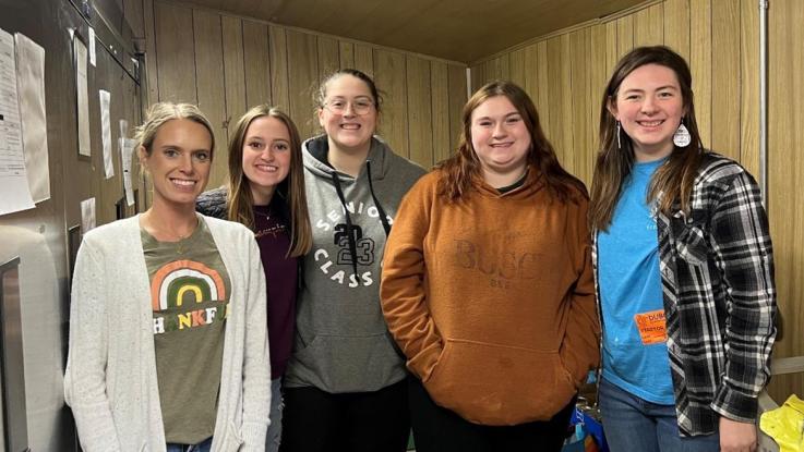 Five students stand in a food pantry storage area.