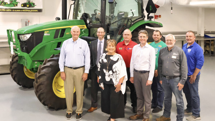 A group of people stand in front of a green John Deere Tractor