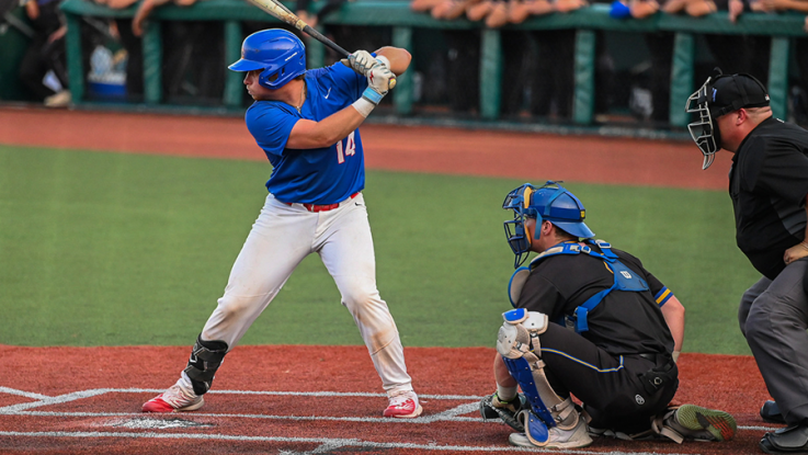 A Loggers baseball player stands ready to bat at the plate, with the catcher and umpire positioned behind.