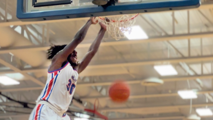 A Loggers basketball player slam dunks a ball and hangs on the rim.