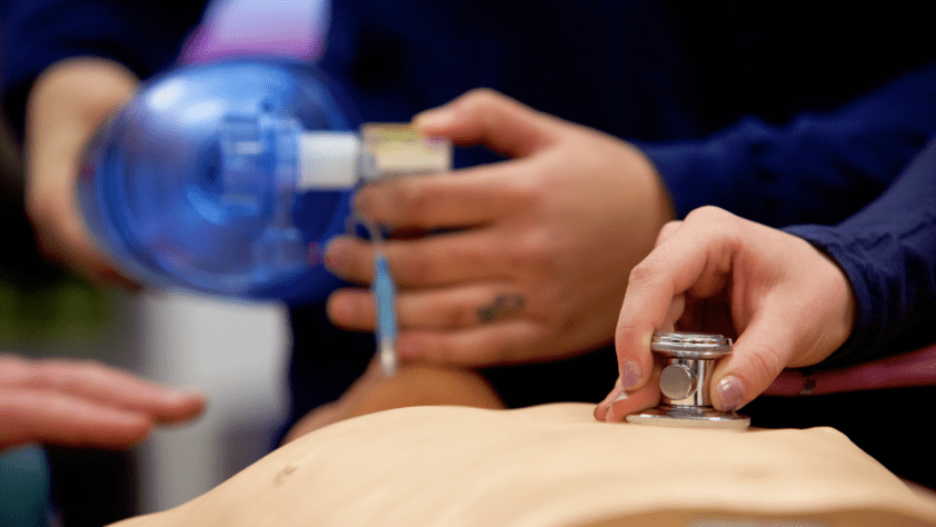 close-up of paramedics working on manikin with stethoscope and giving oxygen