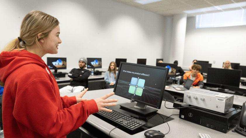 student giving a presentation to the class, with her laptop open that has a document open that says "What makes my product different?"