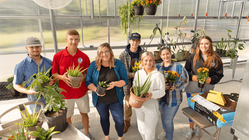 students holding plants inside a greenhouse.