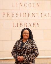 A woman stands in front of sand-colored bricks that are engraved with the words "Lincoln Presidential Library."