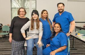 Four students in scrubs pose with their CNA instructor.