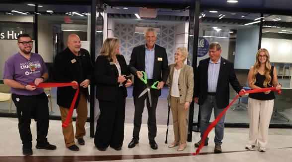 A group of offical staff cut a red ribbon with large green scissors.